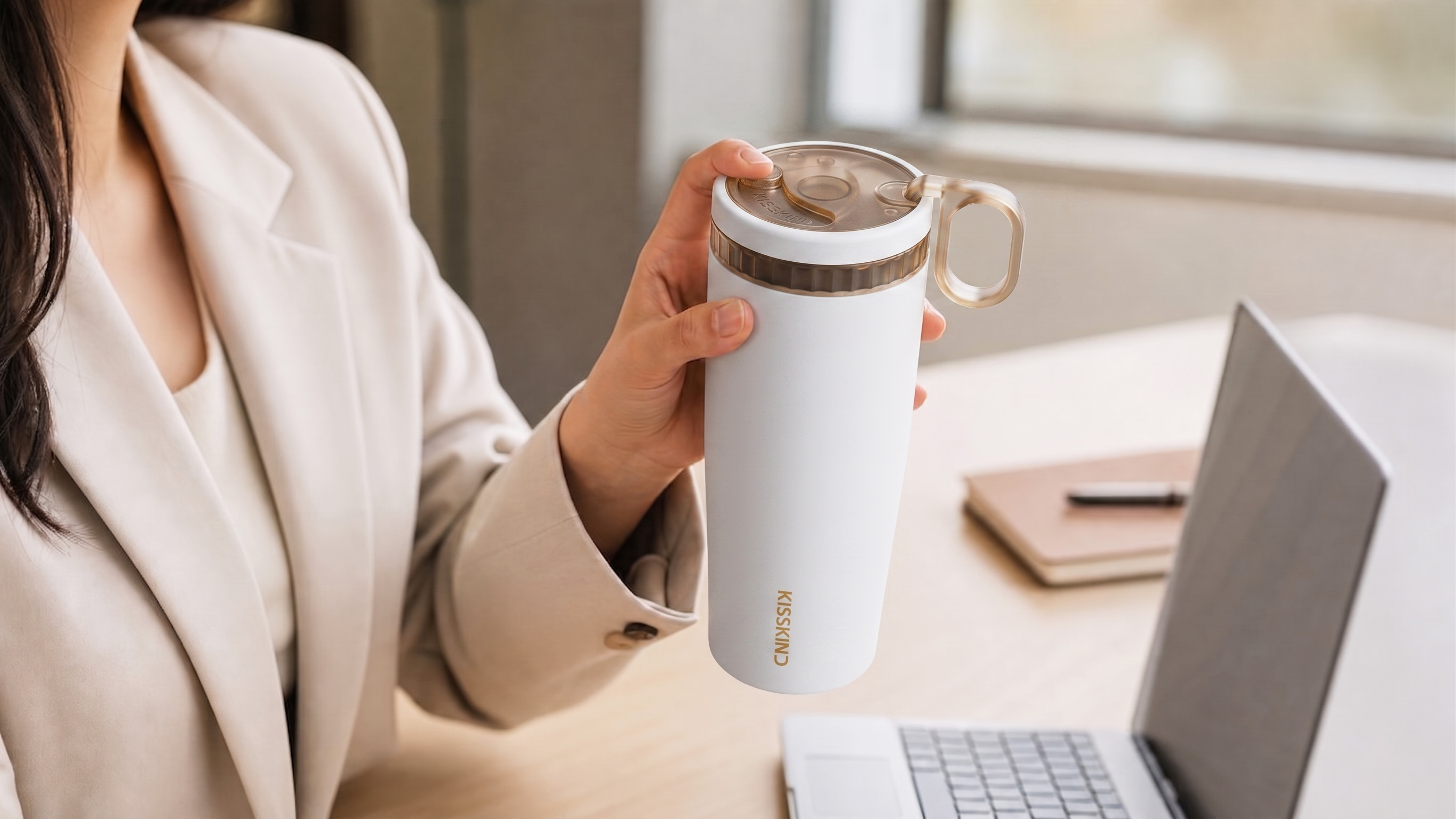 White Kisskind tumbler held beside a laptop at work